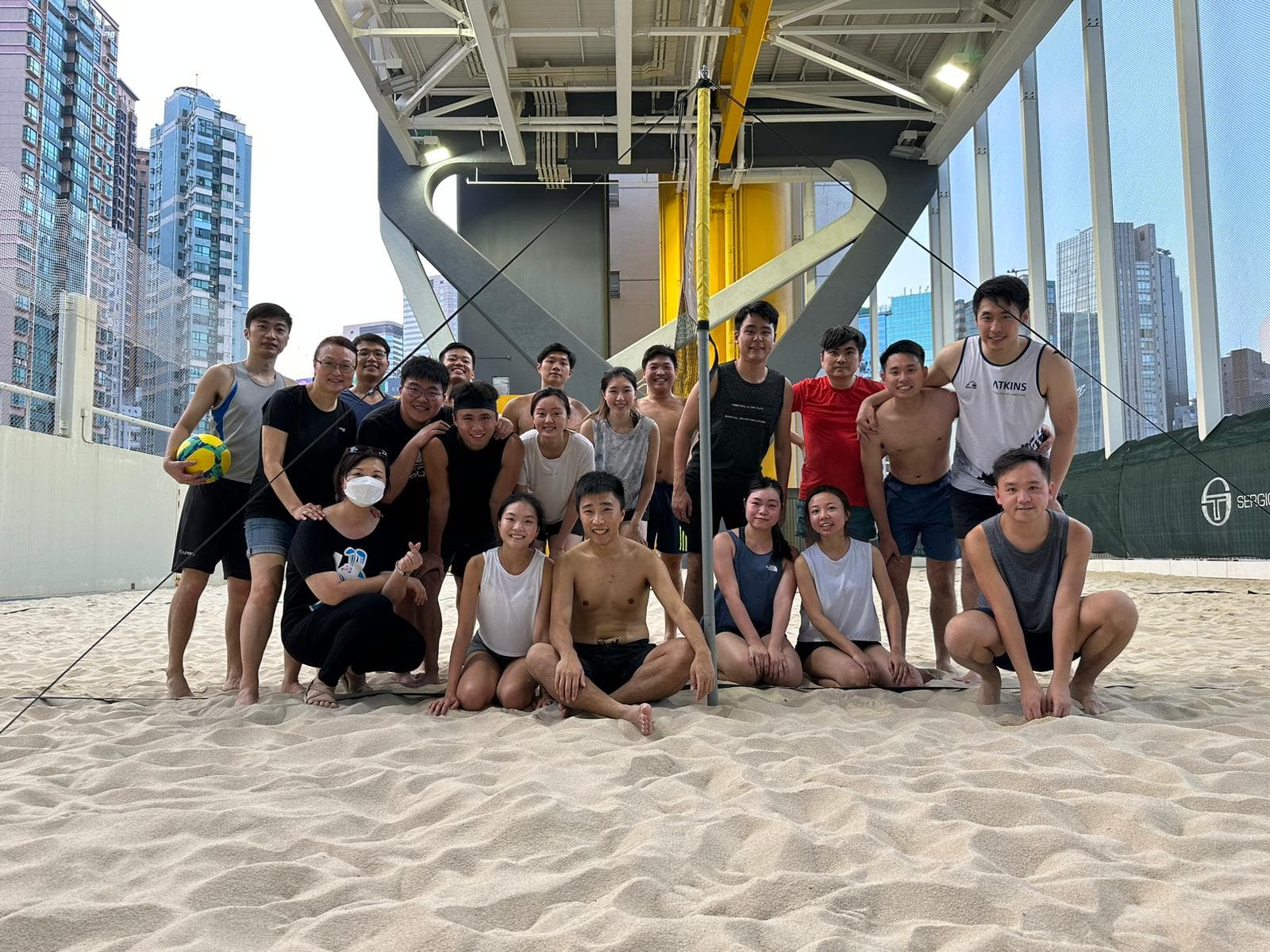 Beach volleyball squad on the sand with the Hong Kong skyline behind them