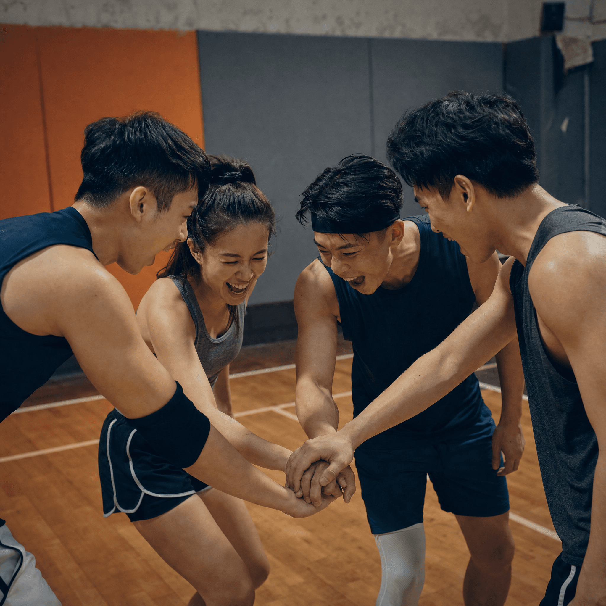 A mixed crew of players in a pre-game hand-stack huddle, laughing, at a Hong Kong sports hall